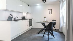 Een moderne keuken met witte kasten, een zwart aanrechtblad en een eethoek met een glazen tafel en zwarte stoelen.