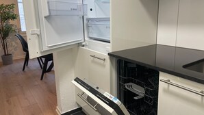Una cocina compacta con armarios blancos, una encimera negra y un lavavajillas.