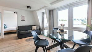 Una sala moderna con una mesa de comedor de vidrio, sillas negras, un sofá y una cama al fondo.