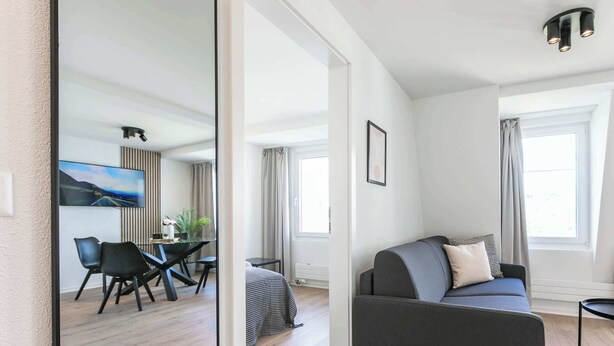 Una sala de estar moderna con un sofá, un comedor con sillas y una mesa, y un ventanal que proporciona luz natural.