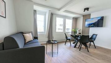 A modern living room with a sofa, dining table, chairs, and a TV mounted on the wall.
