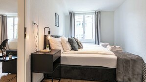Une chambre d’hôtel moderne, équipée d’un lit, d’une table de chevet, d’une lampe et offrant une vue sur la ville par la fenêtre.
