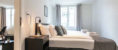 A modern hotel room with a bed, bedside table, lamp, and a view of the city through the window.