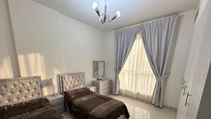 A bedroom with two beds, a nightstand, a dresser, a mirror, and a window with curtains.