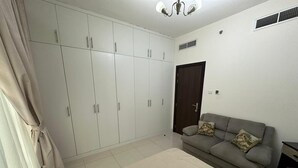A bedroom with a bed, a grey sofa, a wardrobe, and a door.