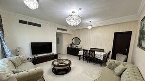 A spacious living room with a large sofa, a round coffee table, a dining table with chairs, and two chandeliers.