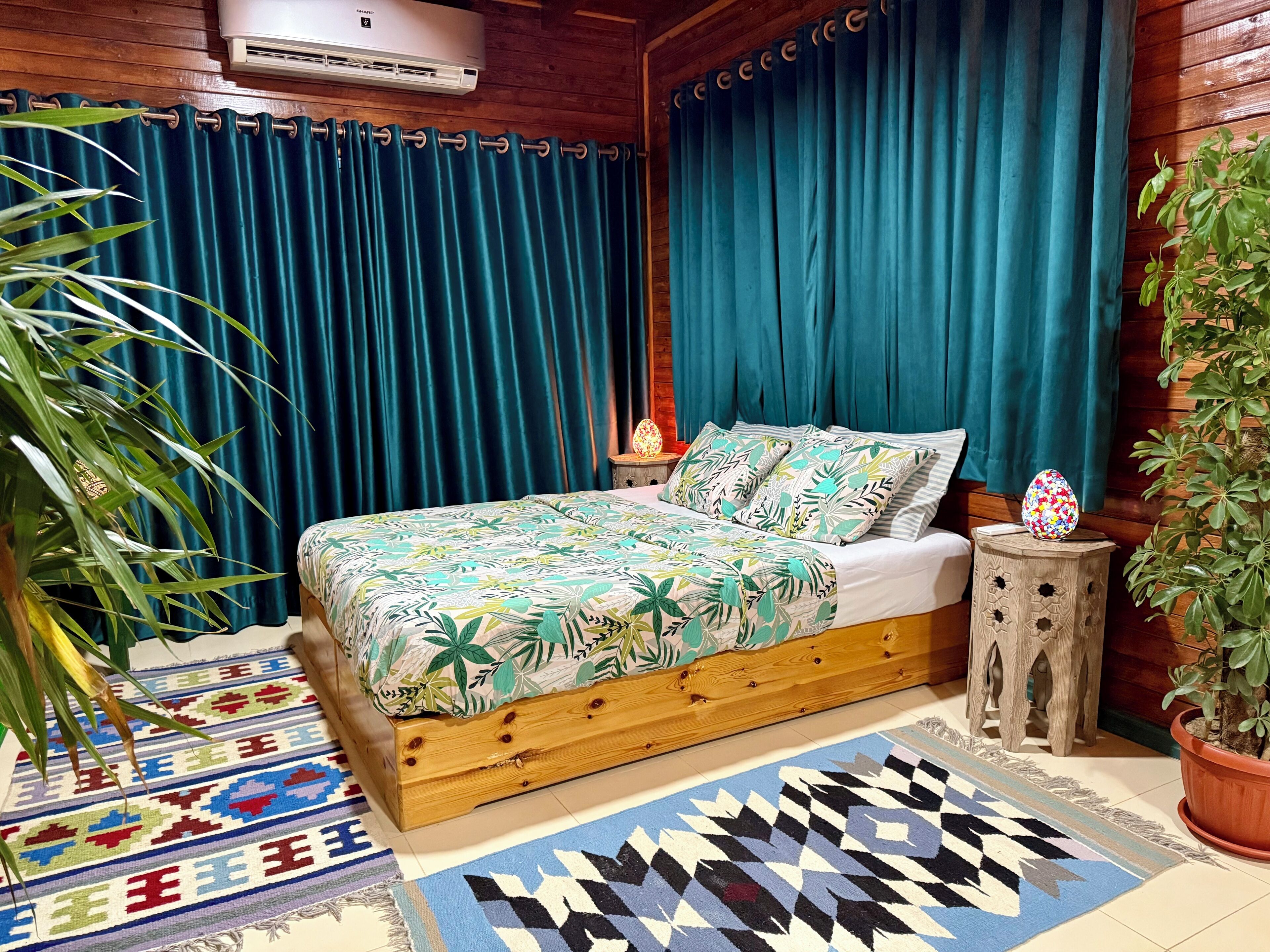 Une chambre à coucher avec un cadre de lit en bois, des rideaux de couleur turquoise, une couvre-lit à motifs et une petite table de chevet avec une lampe.