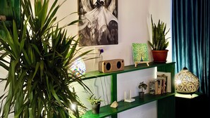 Une pièce dans laquelle se trouve une étagère verte, sur laquelle sont exposés divers objets, notamment une plante en pot, une lampe décorative et une œuvre d’art encadrée.