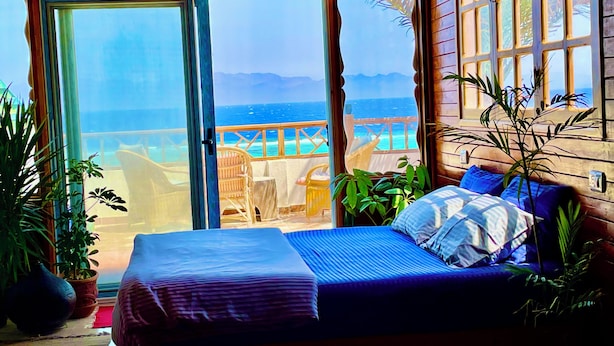 Une chambre avec un lit, une vue sur l’océan et un balcon agrémenté de meubles en osier.