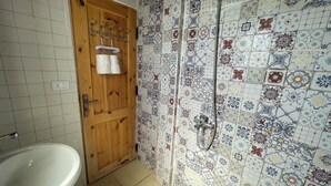 Une salle de bain avec une porte en bois, un lavabo blanc et une douche avec un mur carrelé.