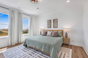 Un dormitorio con una cama grande, dos mesitas de noche con lámparas, vistas al exterior y dos obras de arte en la pared.