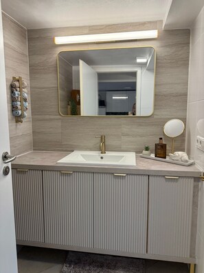 Une salle de bain avec un lavabo blanc, un robinet doré, un miroir et un porte-serviettes.