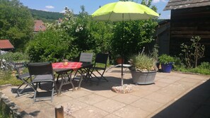 Une terrasse extérieure avec une table et des chaises, une plante en pot et un parasol jaune.