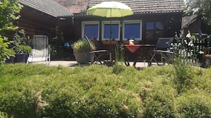 Ein Holzhaus mit Ziegeldach, einer Terrasse mit Tisch und Stühlen sowie Blumentöpfen.