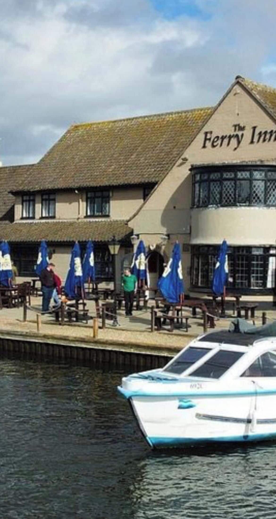 A waterfront building named 'The Ferry Inn' with outdoor seating and a boat docked in the foreground.
