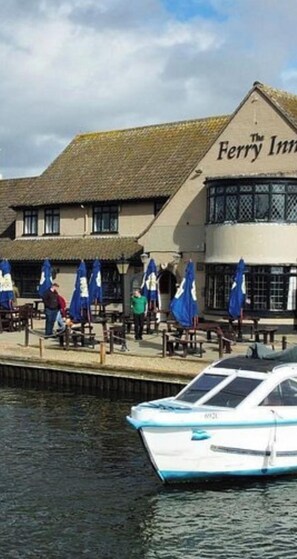 Un bâtiment situé au bord de l’eau, appelé « The Ferry Inn », avec un bateau amarré devant.