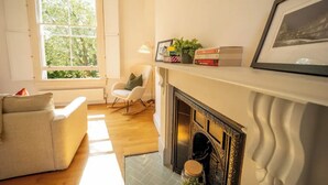 Un salon avec une cheminée, un canapé, un fauteuil et une fenêtre donnant sur la forêt.