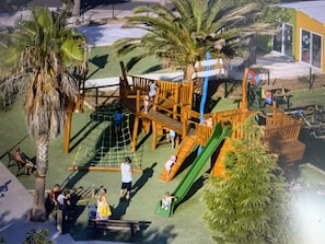 Un parc infantil amb zones de jocs d'escalada, tobogans i una zona protegida per xarxa.