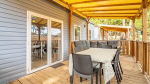 A covered outdoor patio with a dining table and chairs, a sliding glass door, and a wooden deck. - Mobile Home at 5* Camping La Yole in Vendres with Lounge Terrace (Vendres)