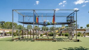 A playground with a climbing structure, swings, and a netted area. - Mobile Home at 5* Camping La Yole in Vendres with Lounge Terrace (Vendres)