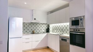 A modern kitchen with white cabinets, a stainless steel refrigerator, a microwave, and an oven.