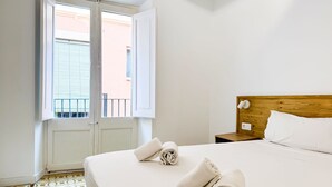 Una habitación de hotel con cama, cabecero de madera, mesita de noche y ventana con persianas.