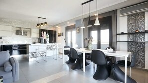 Eine moderne Küche mit Essbereich, ausgestattet mit einem weißen Tisch, schwarzen Stühlen und Pendelleuchten.