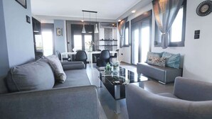 Ein modernes Wohnzimmer mit einer Couch, Sesseln, einem Glastisch und einem Essbereich mit Stühlen.