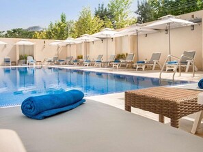 A swimming pool with lounge chairs and umbrellas, a wicker chair, and a blue towel on the edge.