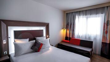 A hotel room with a large bed, a sofa, a bedside table, and a window with curtains.