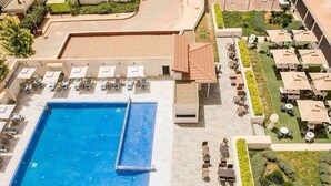 A swimming pool with lounge chairs and tables, surrounded by greenery and a covered patio area. - Rénéa Hotel (Sétif)