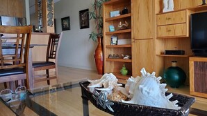 A living room with a glass coffee table, wooden chairs, a wooden bookshelf, and a television. - Oceanfront Paradise Awaits at Kahana Reef 215 (Lahaina)