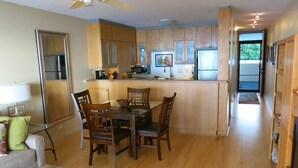 A modern kitchen with wooden cabinets, a central island with seating, a dining table, and a refrigerator. - Oceanfront Paradise Awaits at Kahana Reef 215 (Lahaina)