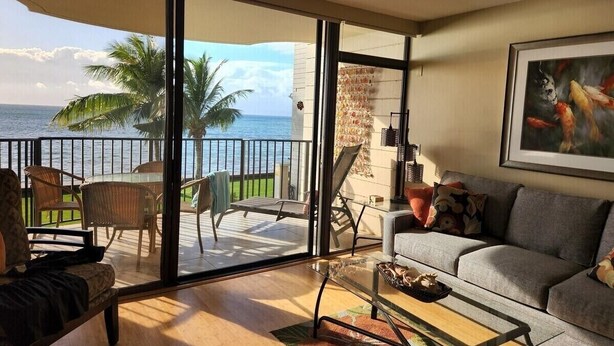 A living room with a sofa, coffee table, and a view of the ocean through large sliding glass doors. - Oceanfront Paradise Awaits at Kahana Reef 215 (Lahaina)