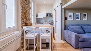 A compact kitchen with white cabinets, a stone accent wall, and a dining area with white chairs. - (034) Le Cocon Méditerranéen (Antibes)