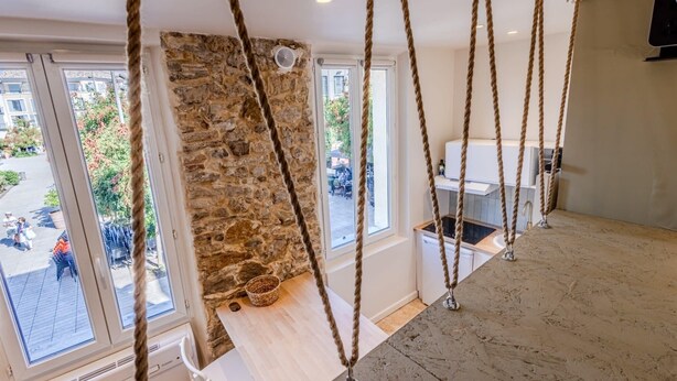 A room with a stone wall, large windows, a wooden bench, and a hanging rope swing. - (034) Le Cocon Méditerranéen (Antibes)