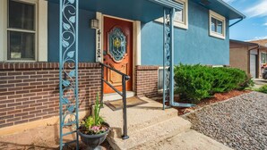 Une maison à l’extérieur bleu, avec une partie inférieure en briques et une porte d’entrée en bois dotée d’une fenêtre en verre.