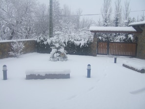 Un espacio al aire libre cubierto de nieve, con un muro de ladrillo, una valla de madera y un pequeño árbol.