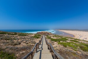 Une promenade en bois qui mène à une plage offrant une vue dégagée sur l’océan et une rive sablonneuse.