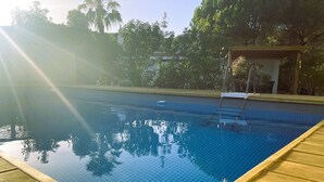Une piscine à eau claire, dotée d’une terrasse en bois, entourée d’arbres et agrémentée d’un espace abrité.