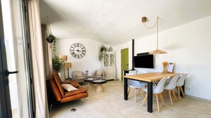 Un salon moderne avec un canapé en cuir marron, une table à manger avec des chaises, une grande horloge murale et un téléviseur fixé au mur.