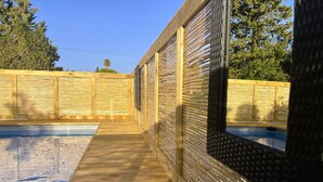 Une terrasse en bois menant à une piscine, le tout bordé d’une clôture en bambou.