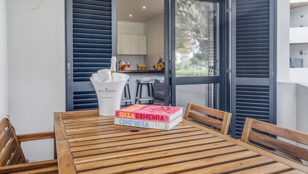 A wooden table with two chairs, a white bucket, and a book titled "IBIZA BOHEMIA" on it. - Sunshine Apartment in Vilamoura (Loulé)