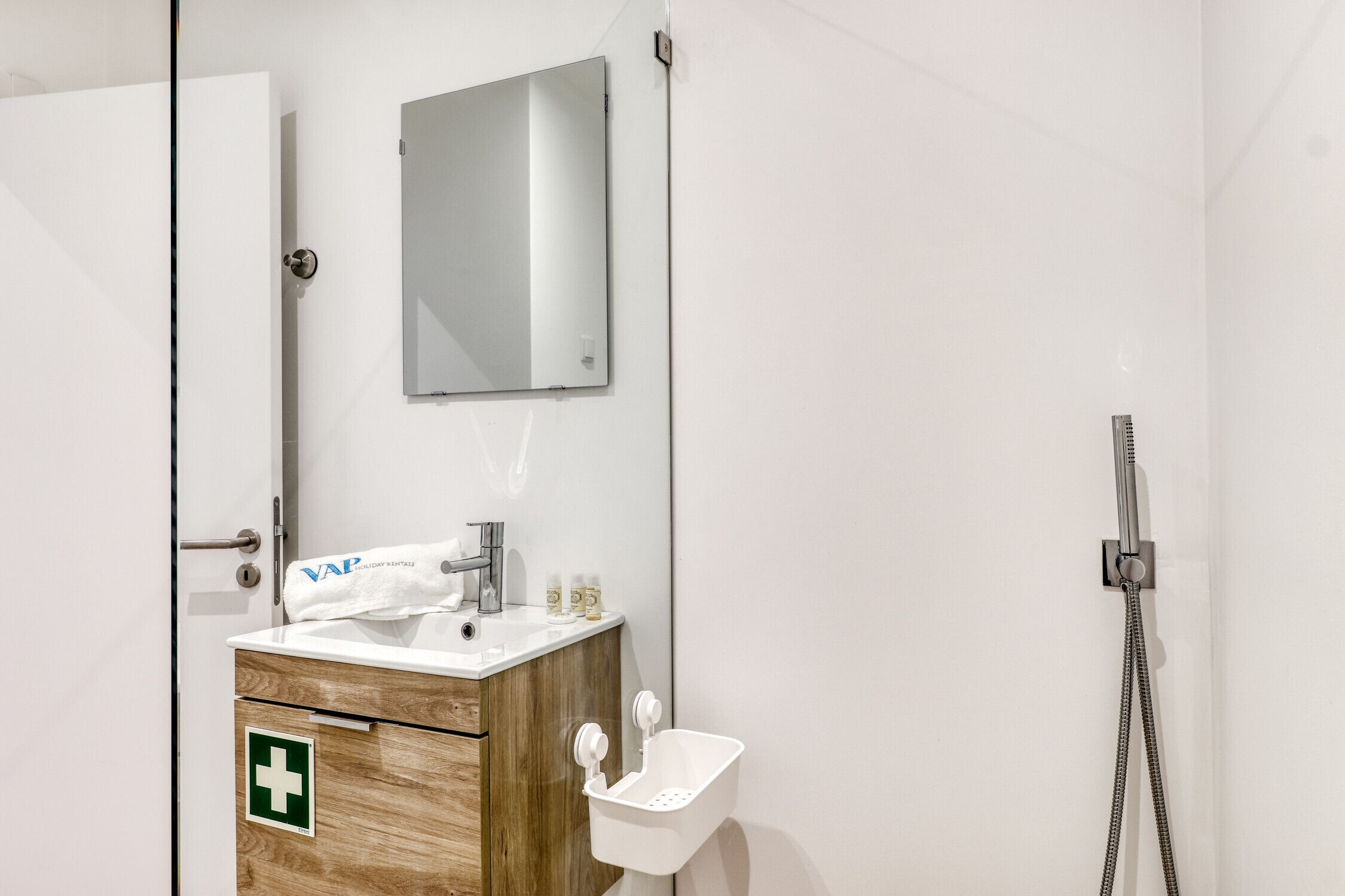 Un baño moderno con tocador de madera, espejo, lavamanos y ducha.