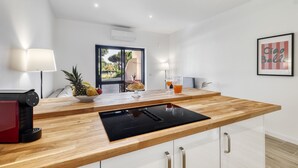 A modern kitchen with a wooden countertop, a black induction cooktop, and a glass backsplash. There is a bowl of fruit and two glasses of orange juice on the counter. - Sunshine Apartment in Vilamoura (Loulé)