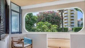 A balcony with a wooden chair, a window with a view of a building and greenery. - Sunshine Apartment in Vilamoura (Loulé)