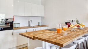 A modern kitchen with white cabinets, a wooden countertop, and a dining area with white chairs. - Sunshine Apartment in Vilamoura (Loulé)