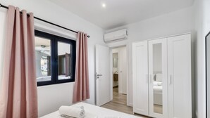 A modern hotel room with a bed, white curtains, an air conditioning unit, and a wardrobe. - Sunshine Apartment in Vilamoura (Loulé)