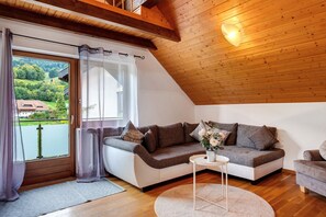 Un salón acogedor con techo de madera, un sofá, una mesita y vistas a un lago.