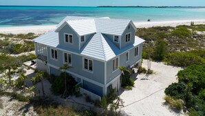A large two-story house with a gabled roof, situated on a sandy beach with a view of the ocean.
